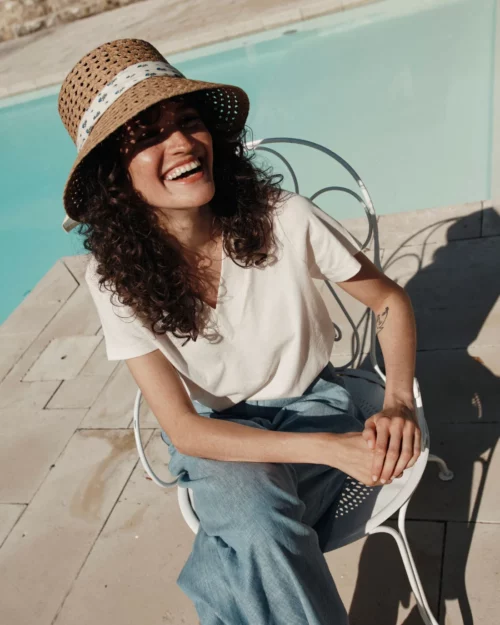 Femme portant le T-Shirt Femme 100% Coton BARRY Emile et Ida crème, associé à un short bleu et un chapeau en paille.
