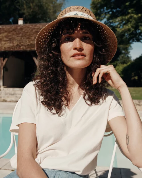 Femme portant le T-Shirt Femme 100% Coton BARRY Emile et Ida crème, assise sur une chaise blanche au bord de la piscine.