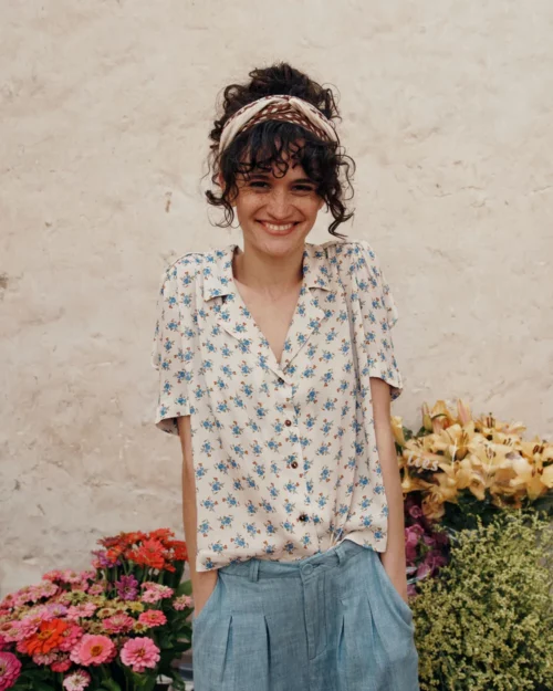Femme souriante portant la Blouse écru fleurs bleues en viscose BOÉMIE Emile et Ida avec un pantalon bleu en lin.