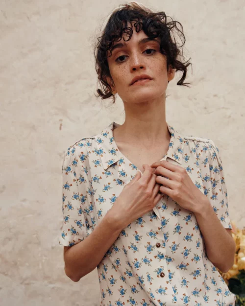 Femme portant la Blouse écru fleurs bleues en viscose BOÉMIE Emile et Ida, boutons ouverts et col légèrement échancré.