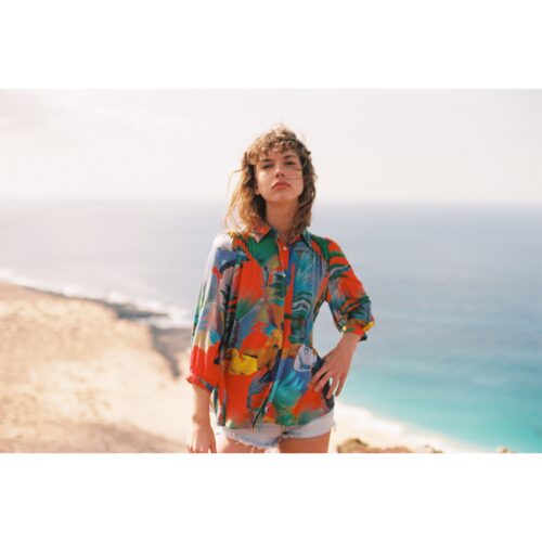 Femme portant la blouse G.KERO KOH KOOD rouge, motifs tropicaux, parfait pour un look estival et décontracté.