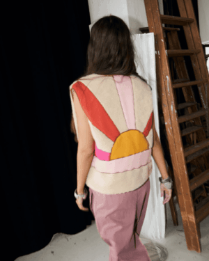 Vu de dos soleil couchant.Veste sans manches.Bouclette.Mouton.Fond écru.Soleil orange et rose.Doublure et extérieur 100%polyester.Jace veste sand